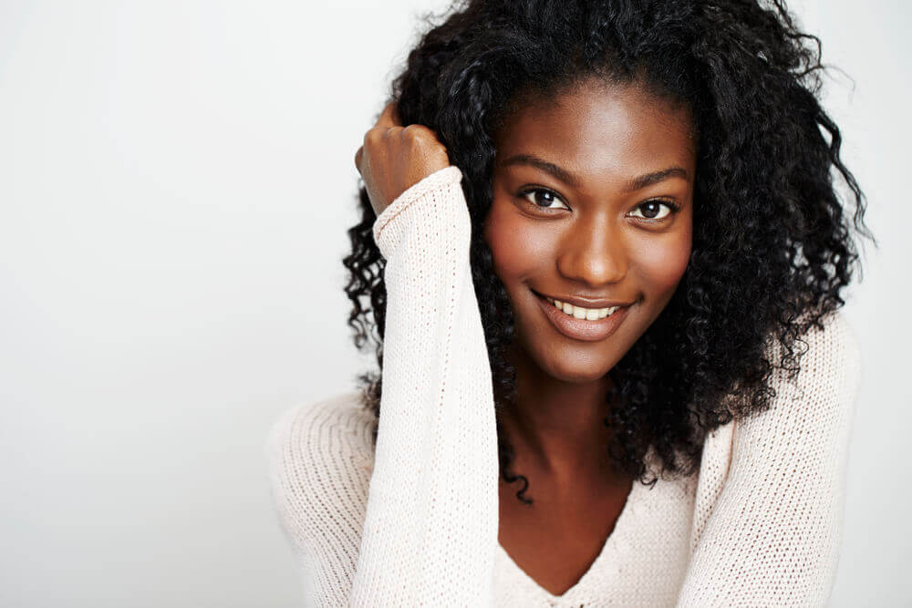 Beautiful young woman with hand in hair smiling at camera