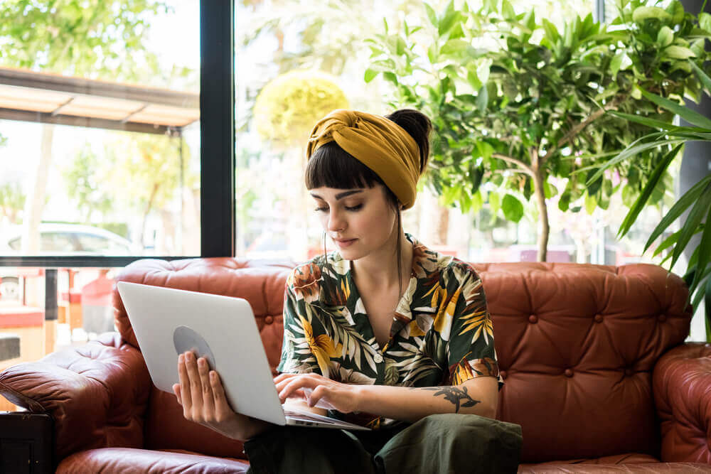 young woman sitting on couch and looking at her laptop