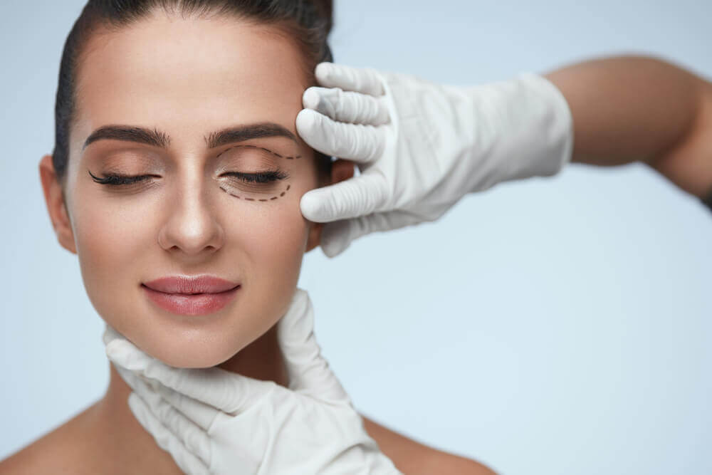 Woman with closed eyes, one eye marked for surgery as gloved hands examine face