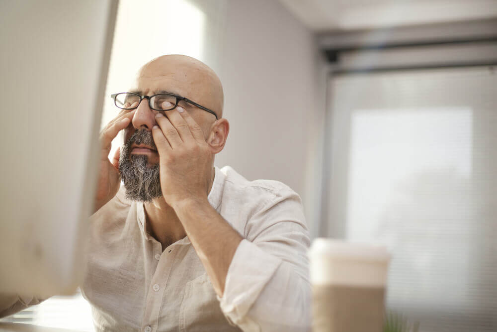Middle-aged man rubbing his eye under his glasses